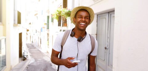 Portrait of a happy male traveler walking in town with mobile phone and bag