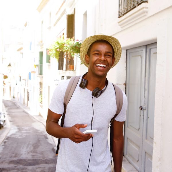 Portrait of a happy male traveler walking in town with mobile phone and bag